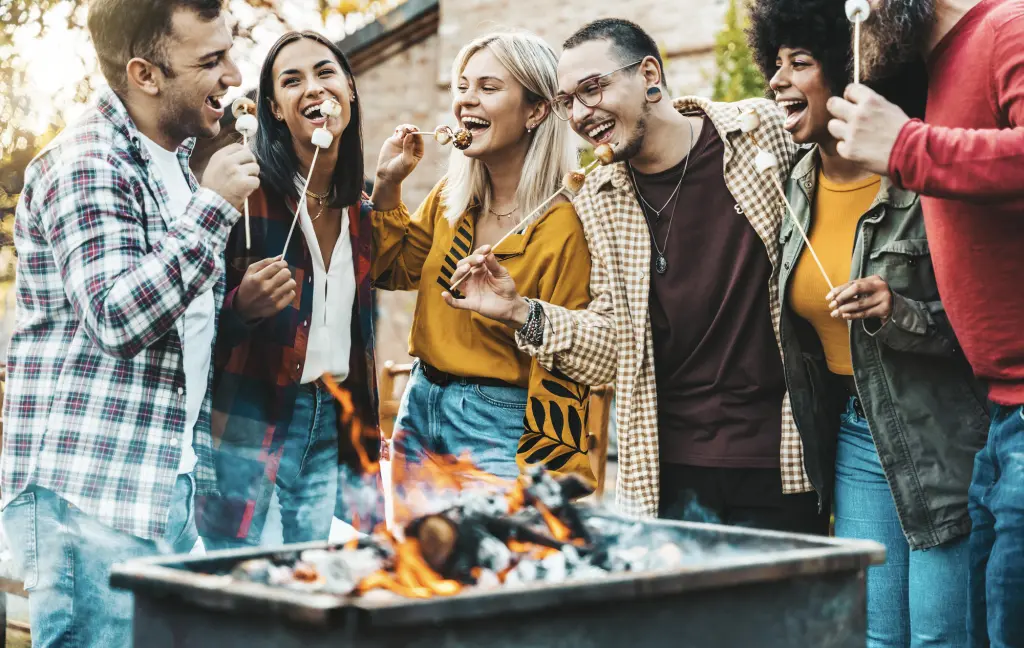 Friends roasting marshmallows over a campfire in the evening